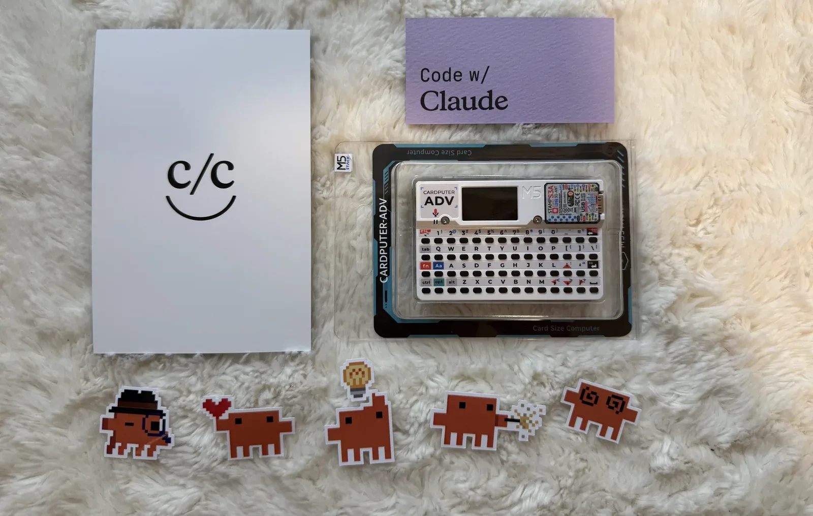 The swag: a c/c card, pixel-art stickers, and an M5Stack Cardputer Adv